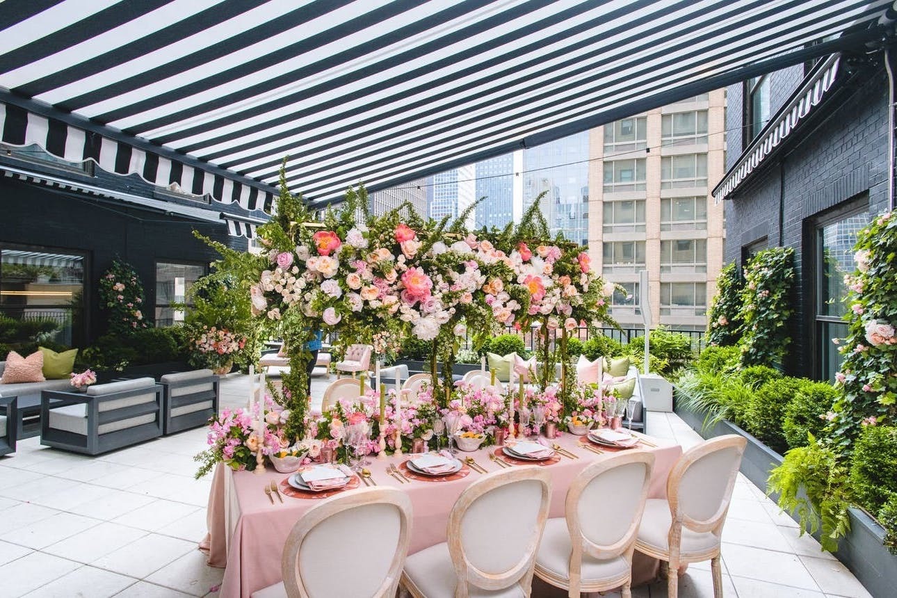 Micro wedding reception table with pink flowers and linens underneath a black-and-white striped canopy at Ivy Terrace