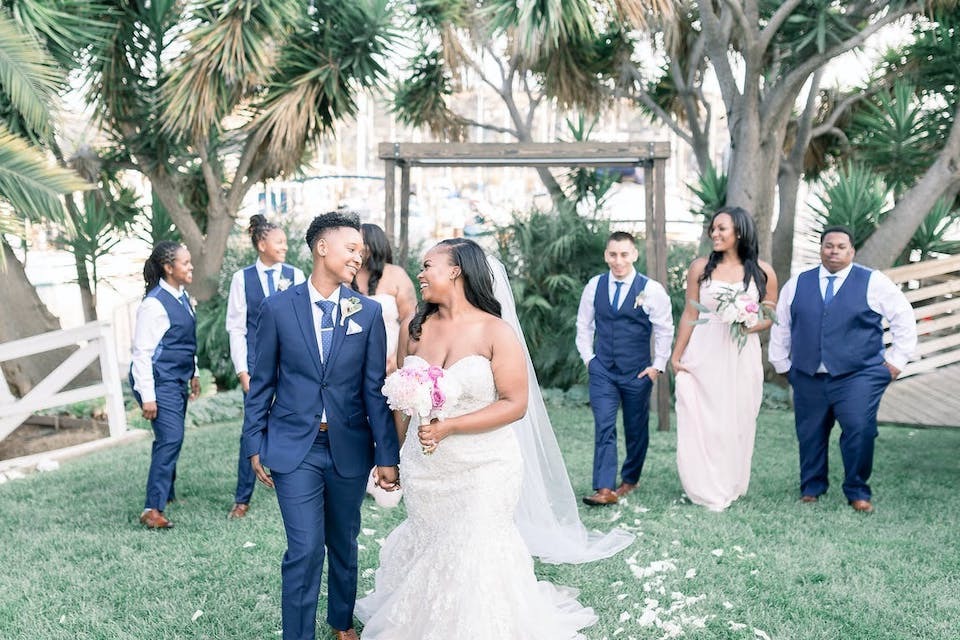 A newlywed couple and happy wedding party walks outside at The Lighthouse at Glen Cove Marina