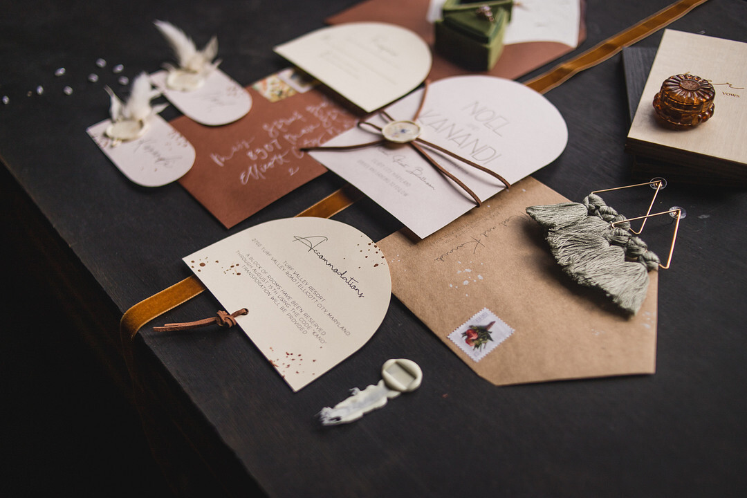 A beautiful boho wedding invitation suite in neutral tones set atop a black tabletop background